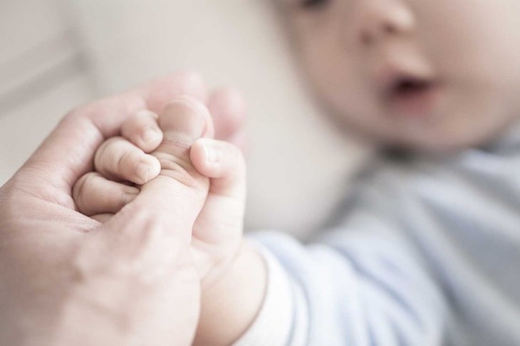 Little newborn baby holding parent's one hand, close-up macro shot. Focus on foreground. The touching and lovely moment. Concept of support, hope, love, bonding and care, hold on...