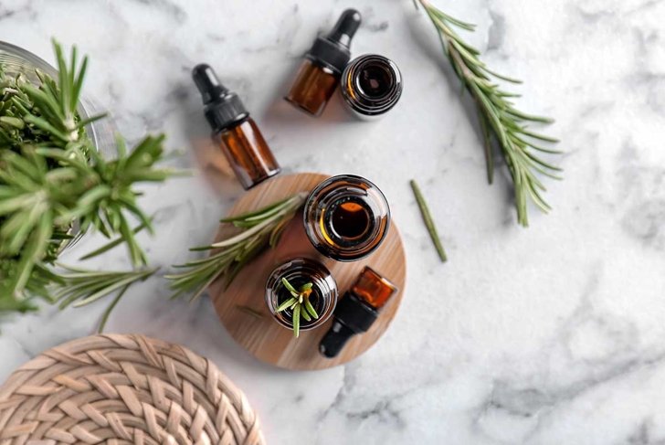 Bottles with rosemary essential oil on light background, top view