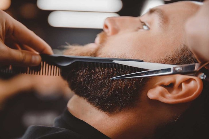 Close-up of barber shearing beard to man in barbershop