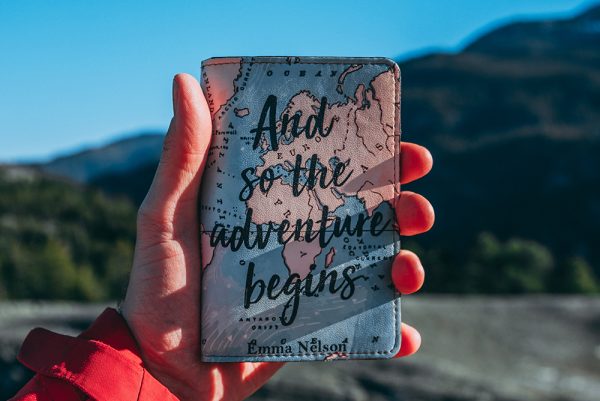 Passport holder with a map on the cover and says, "And so the adventure begins"