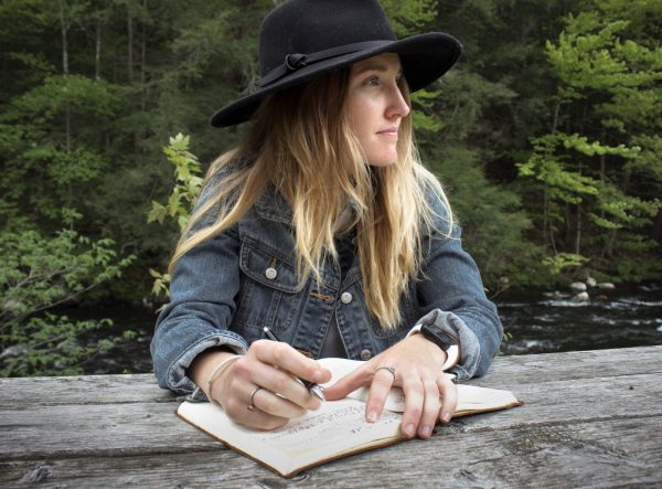 Blonde woman with black hat sitting on a bench with an open journal