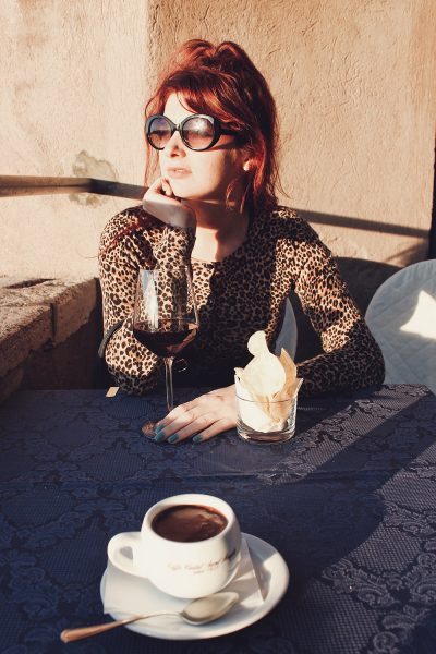 Red-headed woman drinking wine with sun in her face.